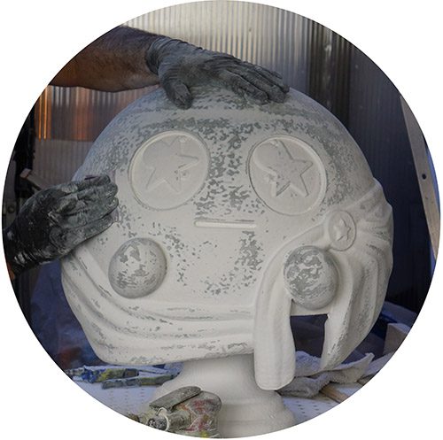 Gloved hands resting on a large white sculpted foam head with star-shaped eyes while the surface coating is worked.