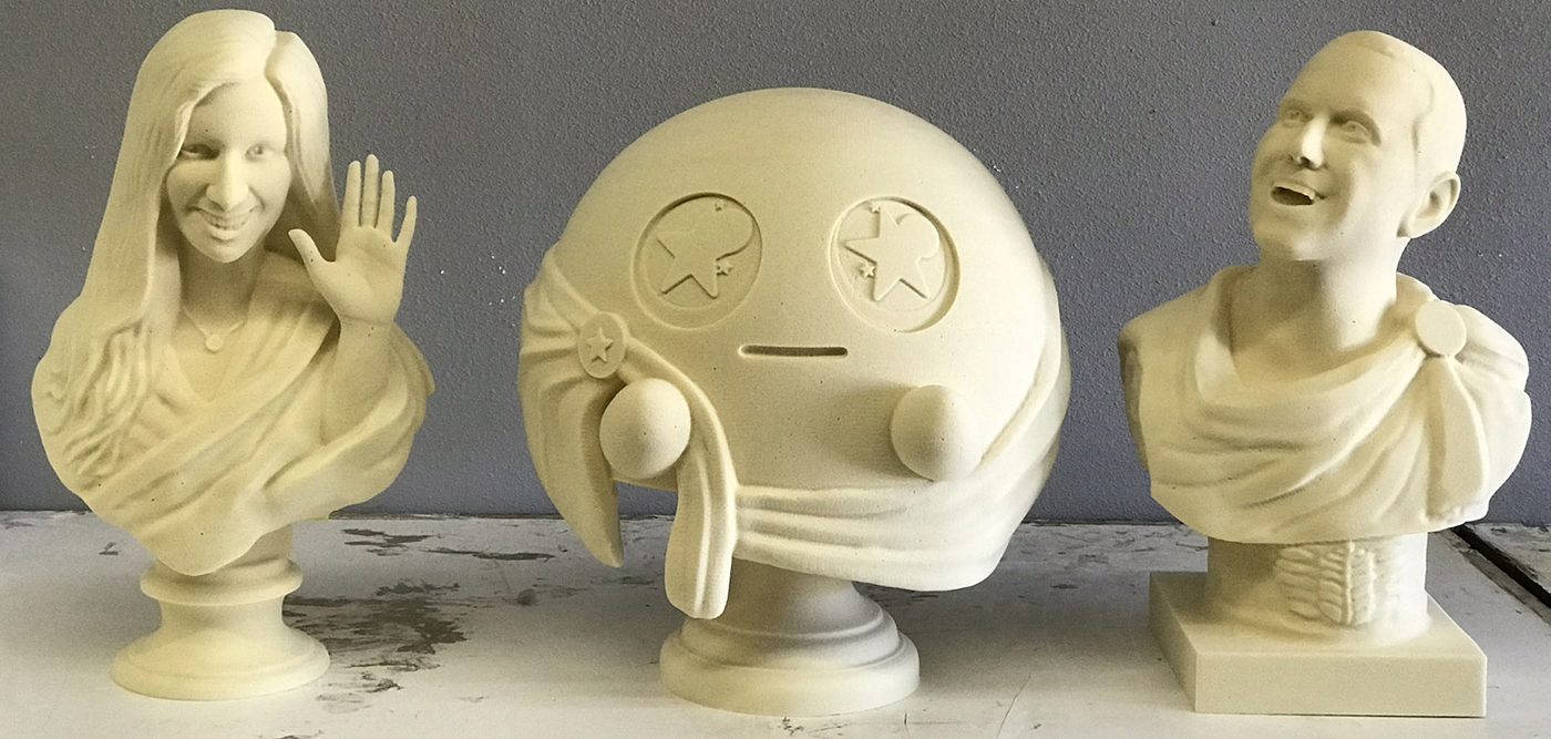 Three cream-colored milled foam sculptures on a shop bench: two busts flanking a round character head with star eyes.