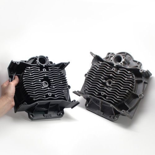 Two black engine housings with cooling fins on a white background, one held in a hand, showing an original and its duplicate.