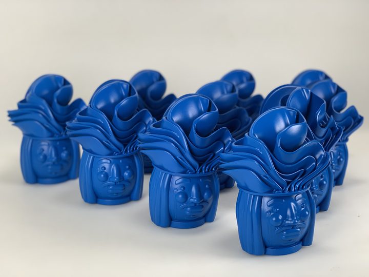 Group of ten matching blue-painted character head sculptures with sculpted hair arranged in rows on a white surface