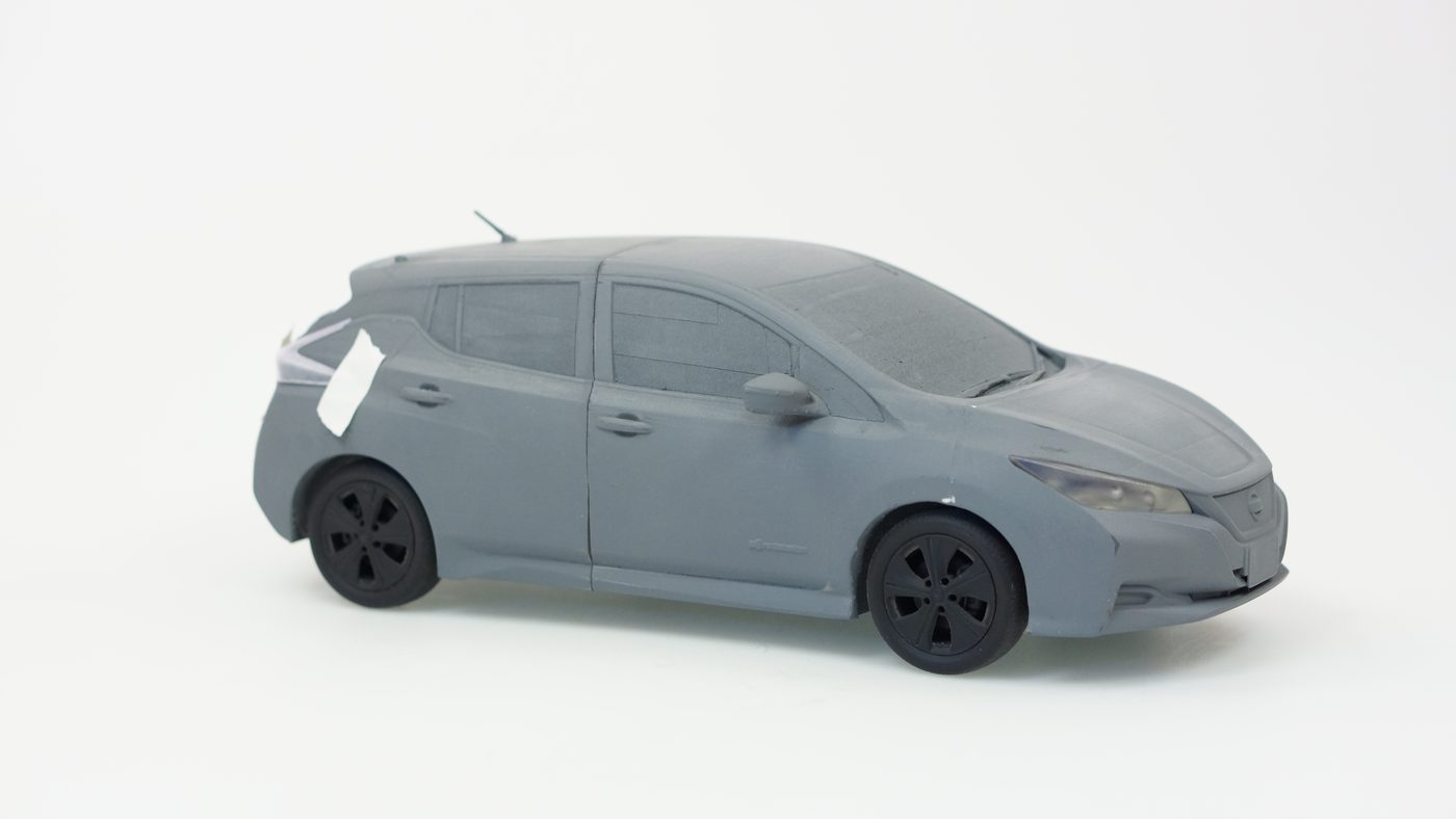 Gray unpainted 3D printed hatchback scale model with black wheels and masking tape on the rear, on a white background