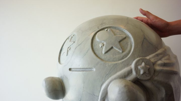 Close view of a large marble-look painted sculpture with embossed star emblems, with a hand resting on top for scale