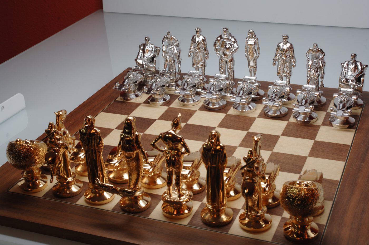 Custom chess set on a wooden board with chrome-silver figure pieces on one side and gold-plated figure pieces on the other
