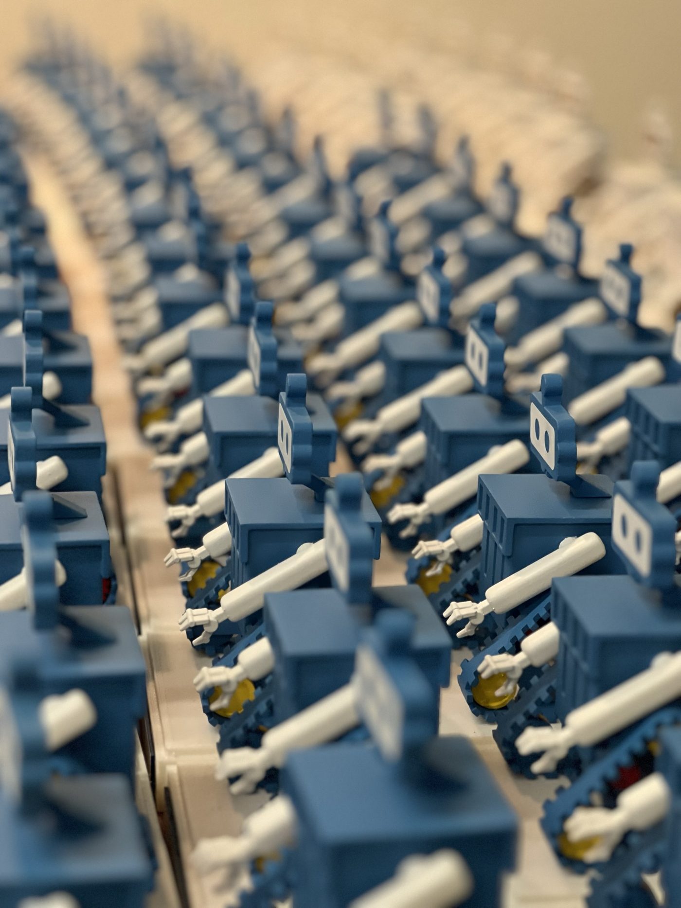 Long rows of small blue and white robot figures with tank treads, sharply focused in the foreground and blurred into the distance