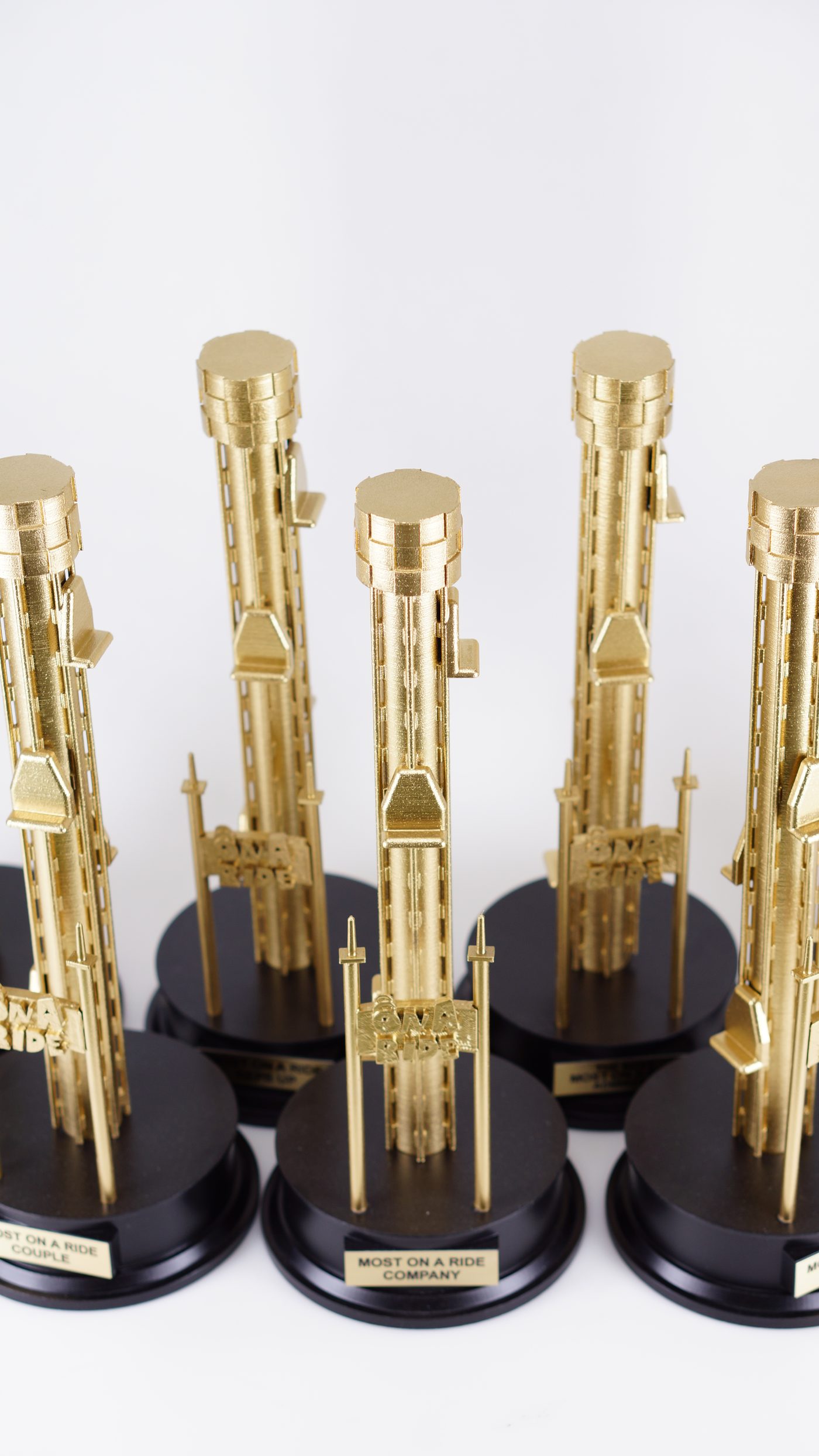 Six matching gold sculptural trophies on black round bases, each with a small gold nameplate reading a different award category