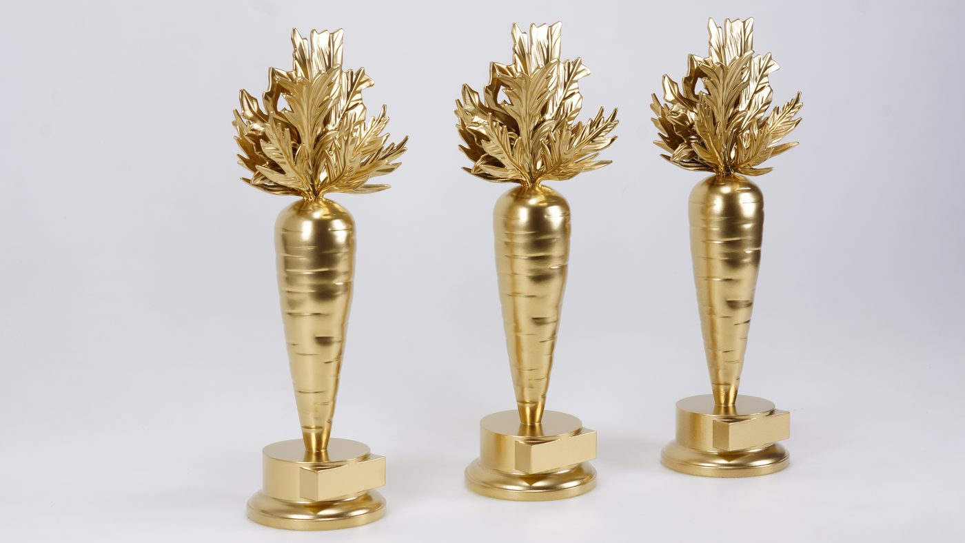Three matching satin gold carrot-shaped trophies with sculpted leafy tops on stepped round bases against a plain white background